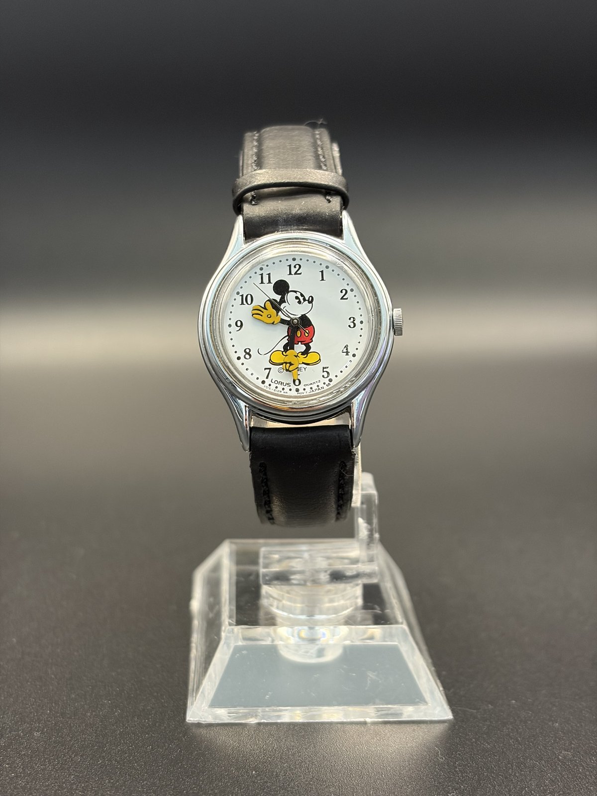 Lorus Mickey Mouse V515-6128 quartz watch on a black leather strap, front view on a stand