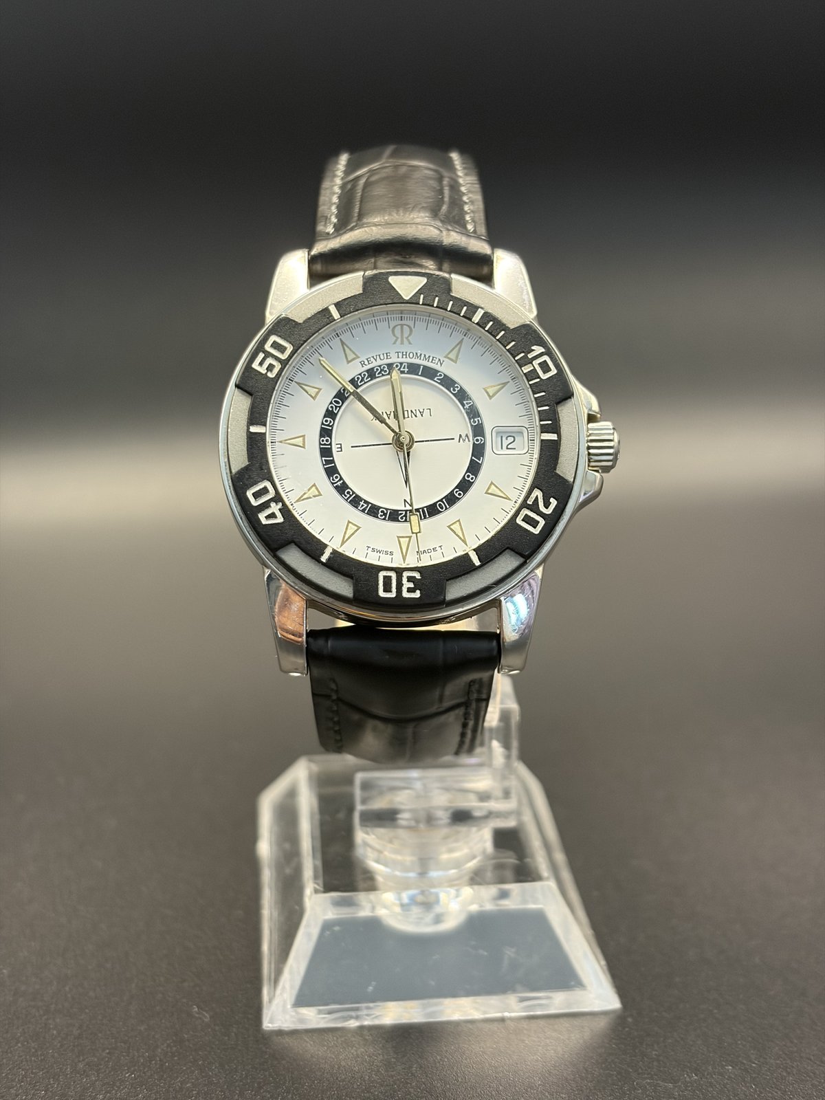 Revue Thommen Landmark Swiss watch with black bezel, white dial and 24-hour ring, front view on a stand