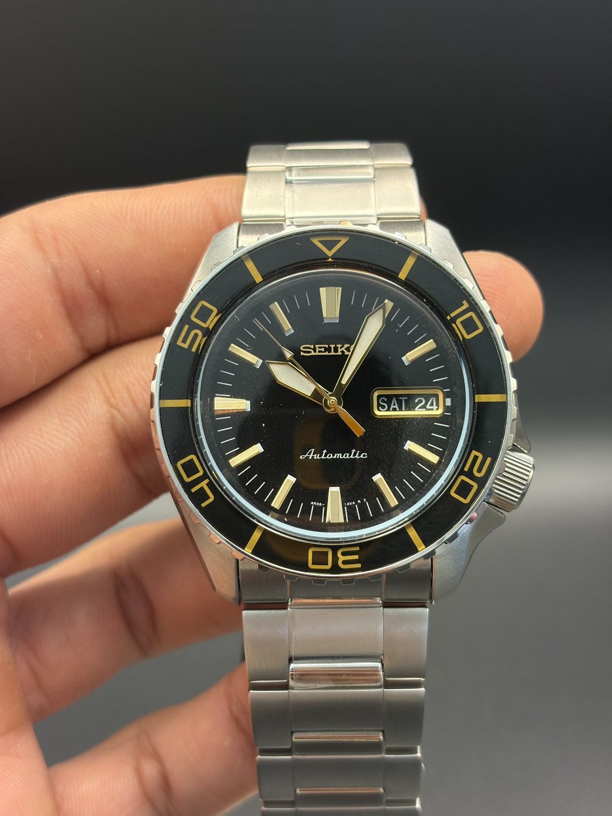 Seiko 5 Sports SRPK99K1 automatic watch with black dial and gold accents, held in hand