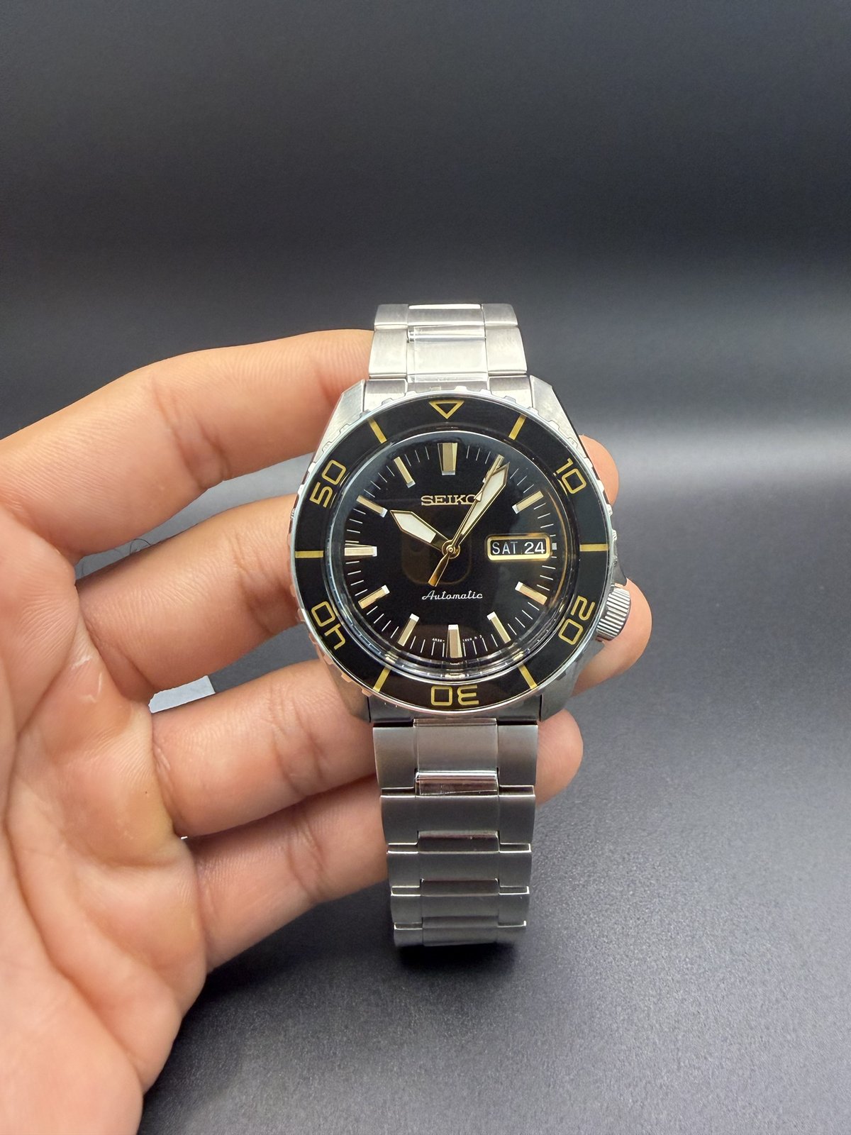 Seiko 5 Sports on a steel bracelet, held in hand